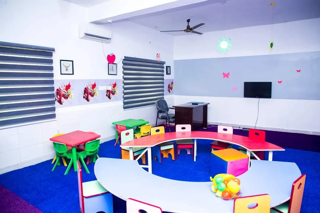 A kindergarten room with a curved table, small chairs and a blue carpet