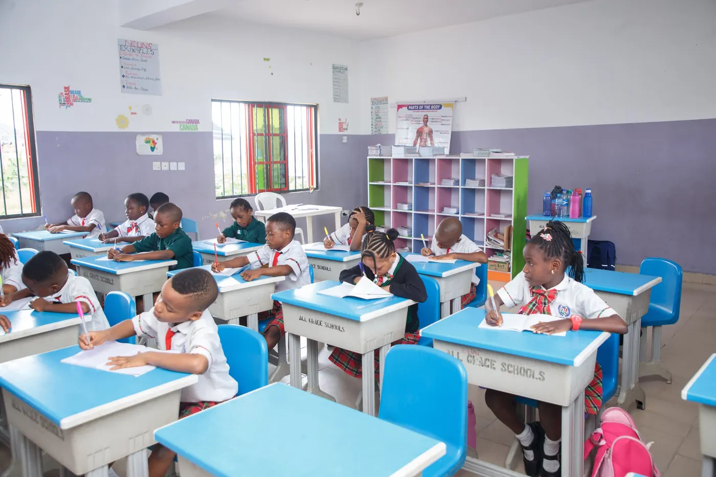 Pupils in uniform writing at blue desks in a bright classroom