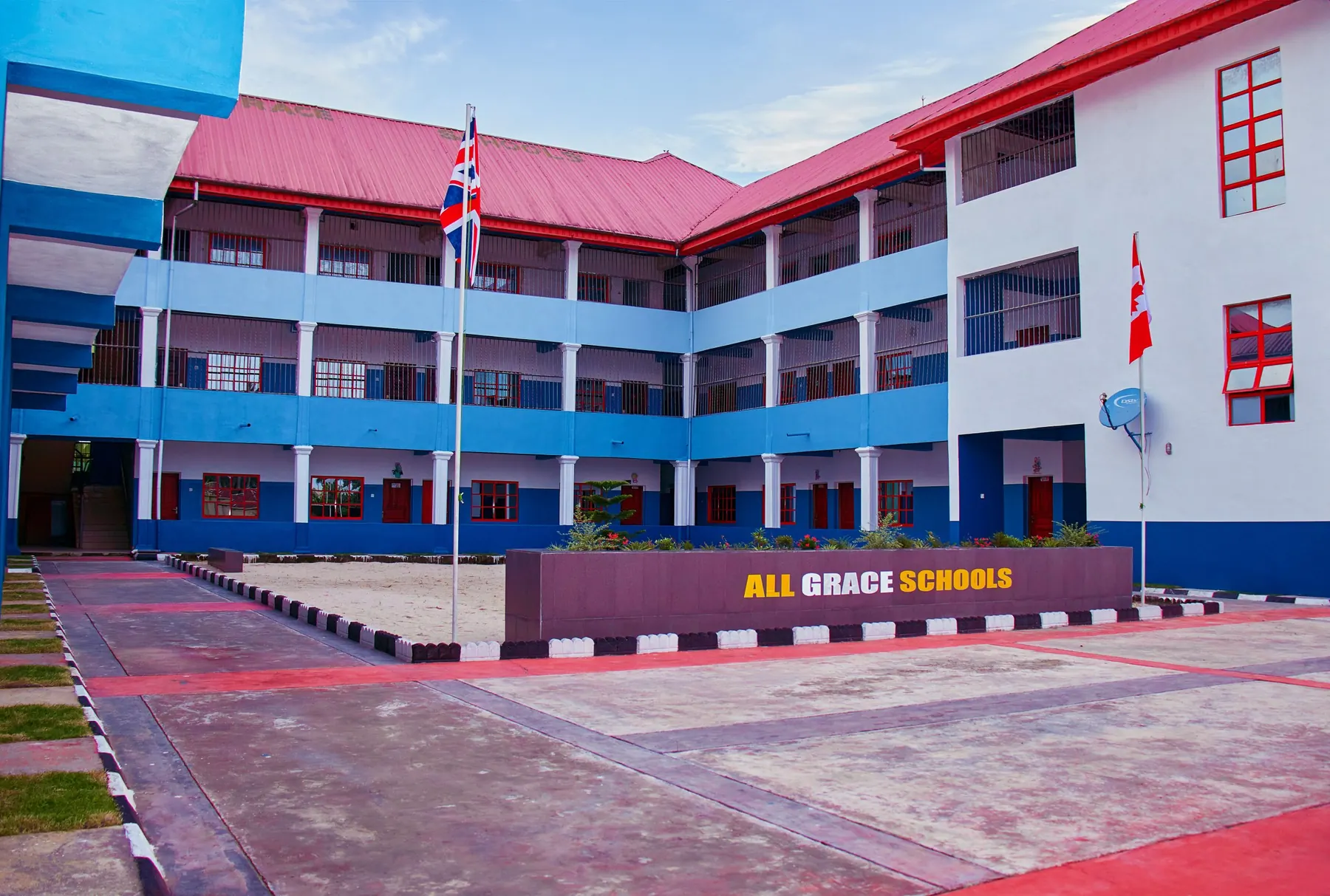 The All Grace Schools building, a three-storey blue and white block with a red roof, seen from the forecourt